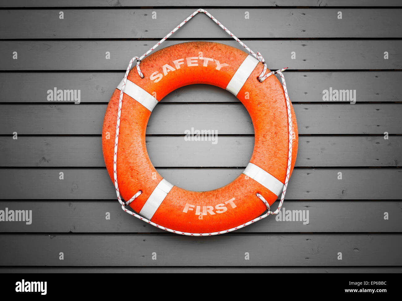La sicurezza prima di tutto. Ciambella rosso con testo etichetta appesa sul grigio parete in legno di un edificio di porta Foto Stock