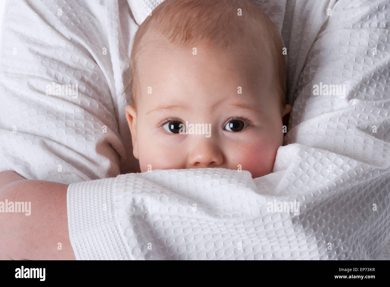 Baby boy con grandi occhi marroni nascondendo in madri di armi Foto Stock
