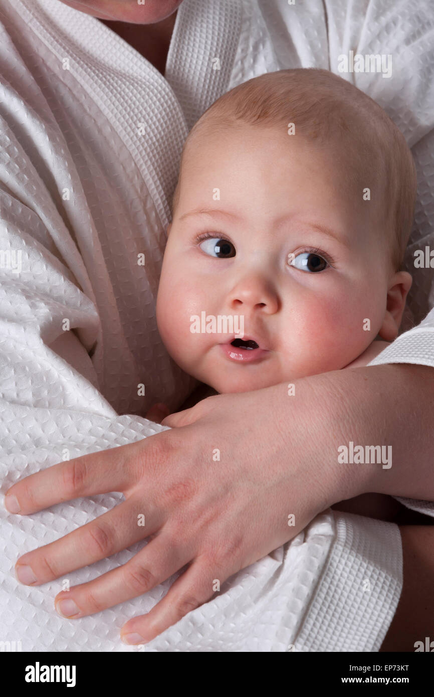 Baby boy con grandi occhi marroni nascondendo in madri di armi Foto Stock