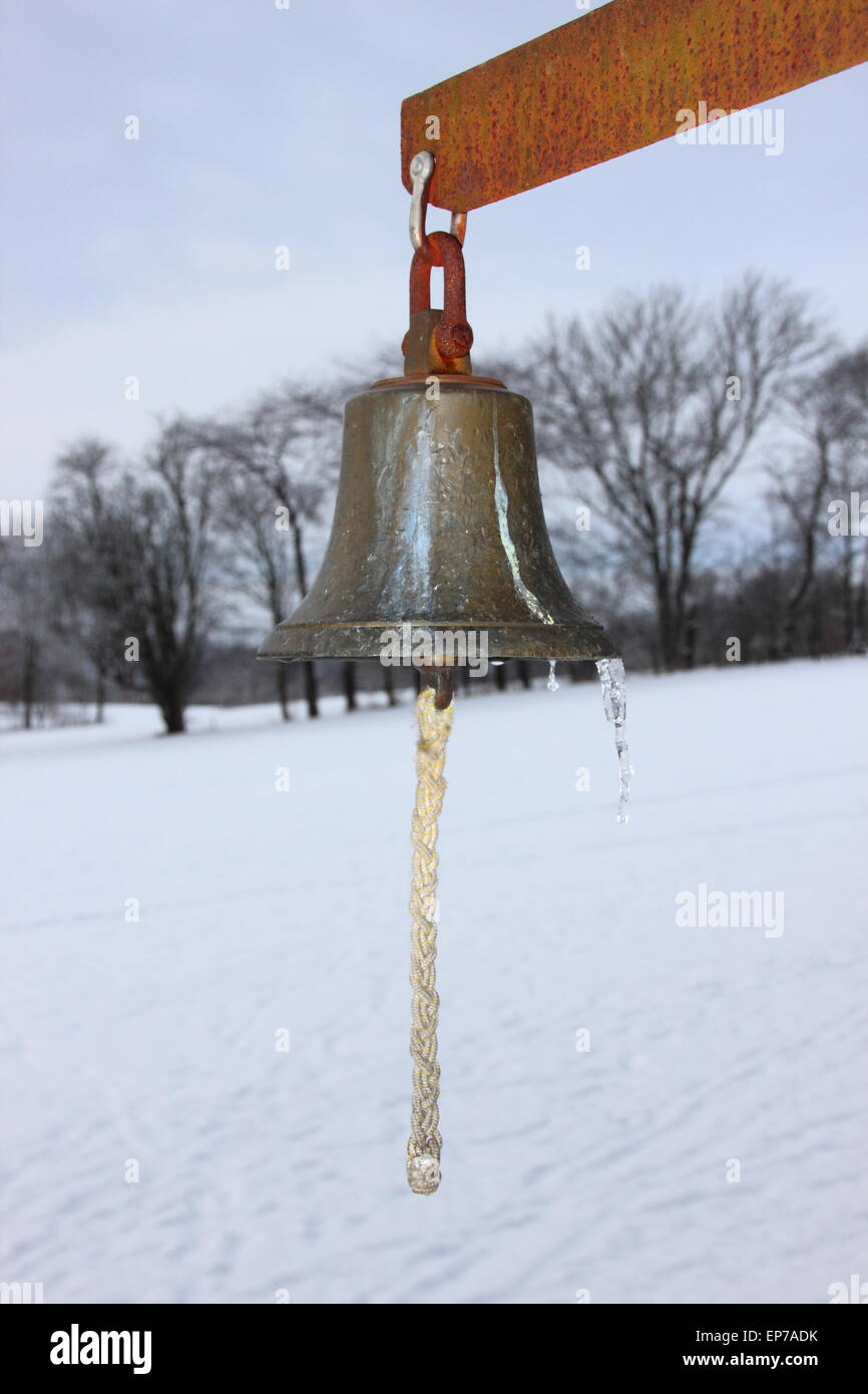 Campana di metallo con inverno campi innevati in background. La campana viene utilizzato su un campo da golf. Foto Stock