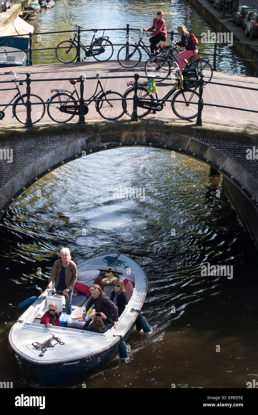 Amsterdam Reguliersgracht Canal con una piccola barca e turisti sul noleggio di biciclette aventi difficoltà escursioni in bicicletta su di una ripida bridge. Foto Stock