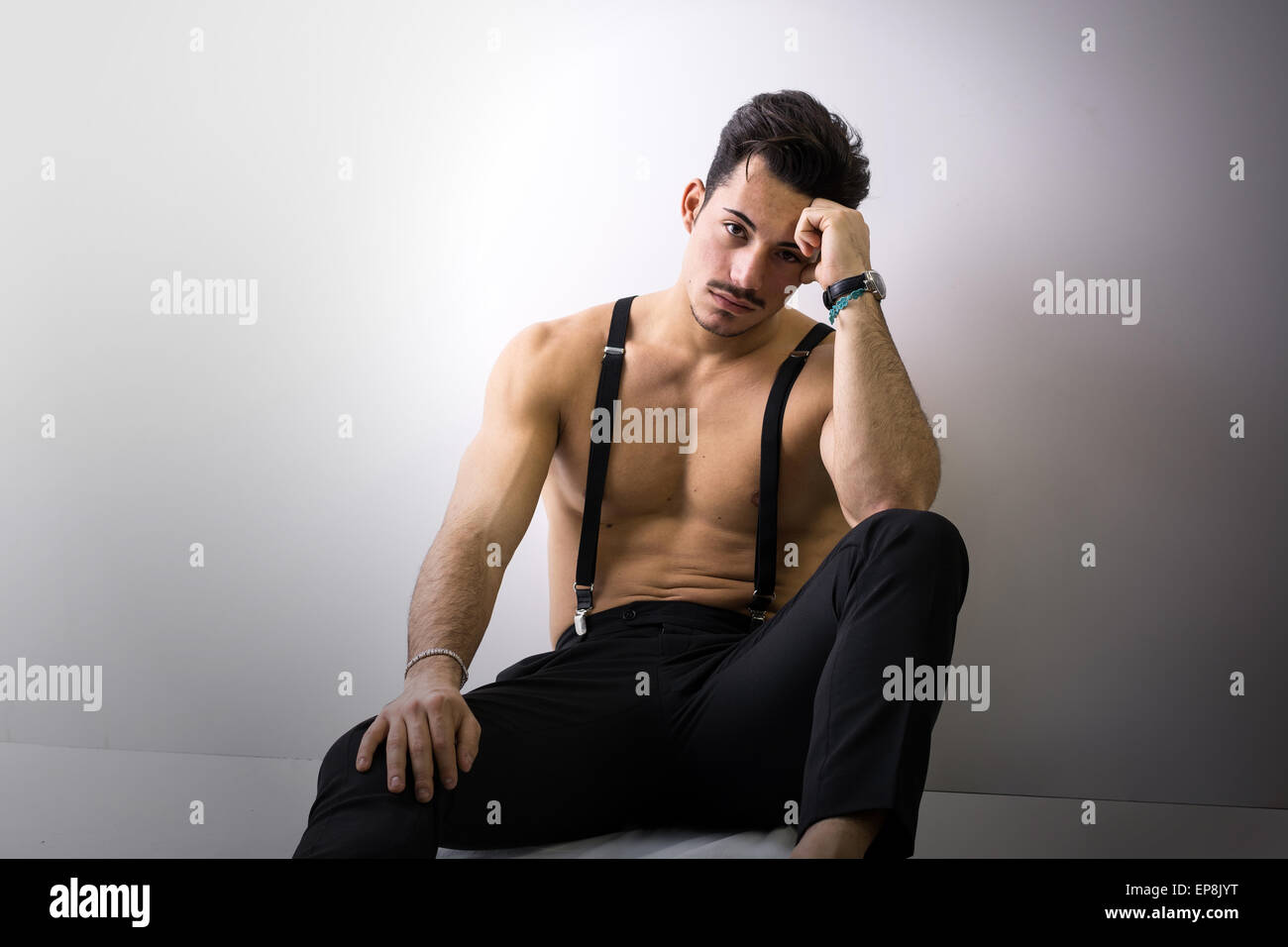 Shirtless athletic giovane con bretelle e pantaloni neri seduto sul  pavimento, guardando la fotocamera Foto stock - Alamy