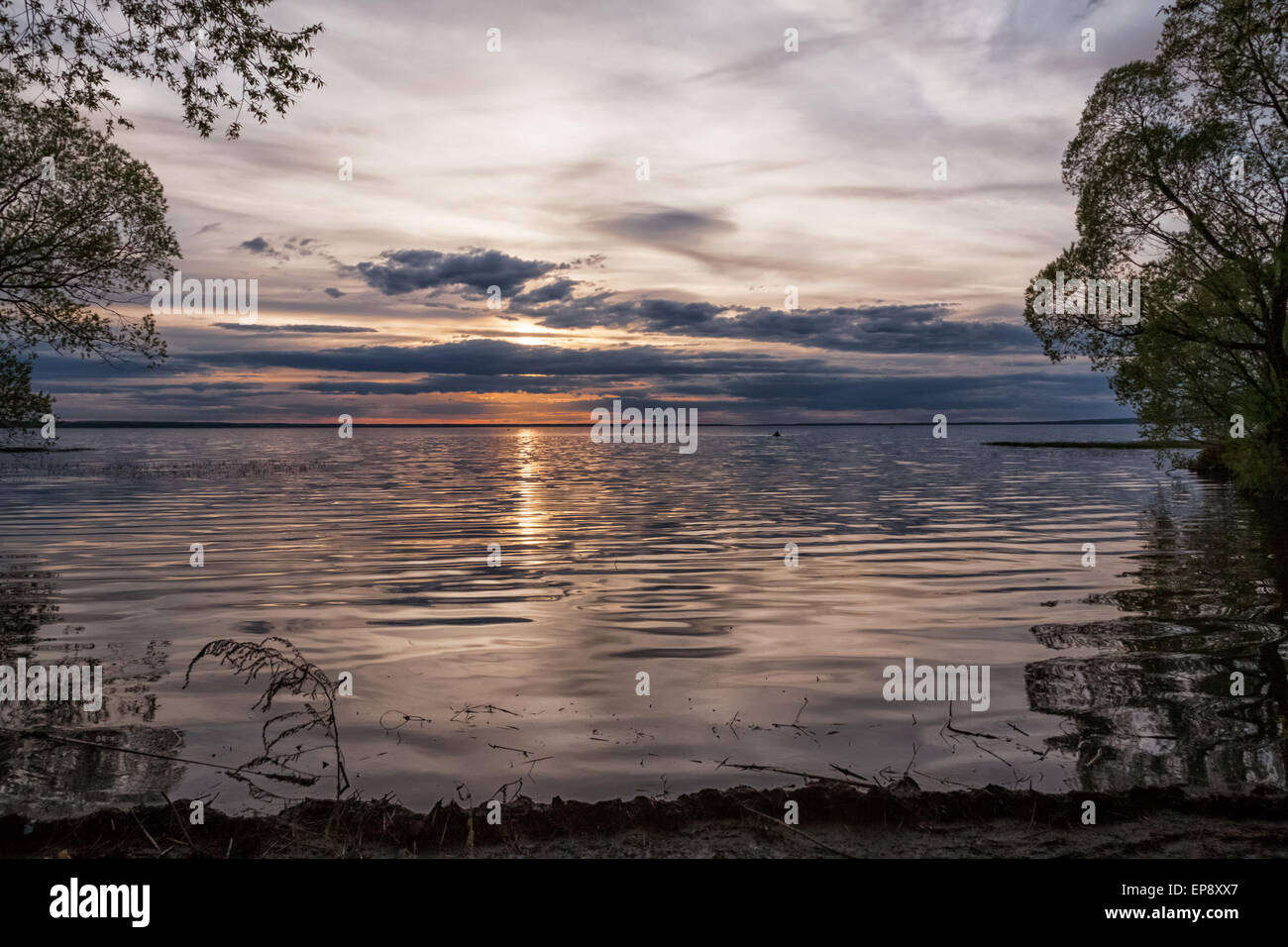 Tramonto a strati su un grande lago di acqua dolce con barche da pesca a distanza Foto Stock