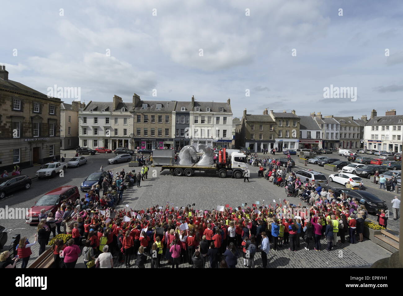 Kelso, Scotland, Regno Unito. Il 15 maggio 2015 tre metri Kelpies elevata per essere stabulati in Kelso quadrato di un decimo di scala touring Kelpies sculture di arrivare in piazza a Kelso venerdì 15 maggio, con studenti locali da Broomlands e Edenside scuole primarie accogliente il loro arrivo. L'iconico sculture rimarrà in posizione al centro della città fino a lunedì 18 maggio. Ciò coincide con un weekend intenso in città e con il castello di pavimenti Horse Trials e la frontiera Vintage associazione agricola annuale del rally a Springwood Park di prendere posto. Credito: Rob grigio/Alamy Live News Foto Stock