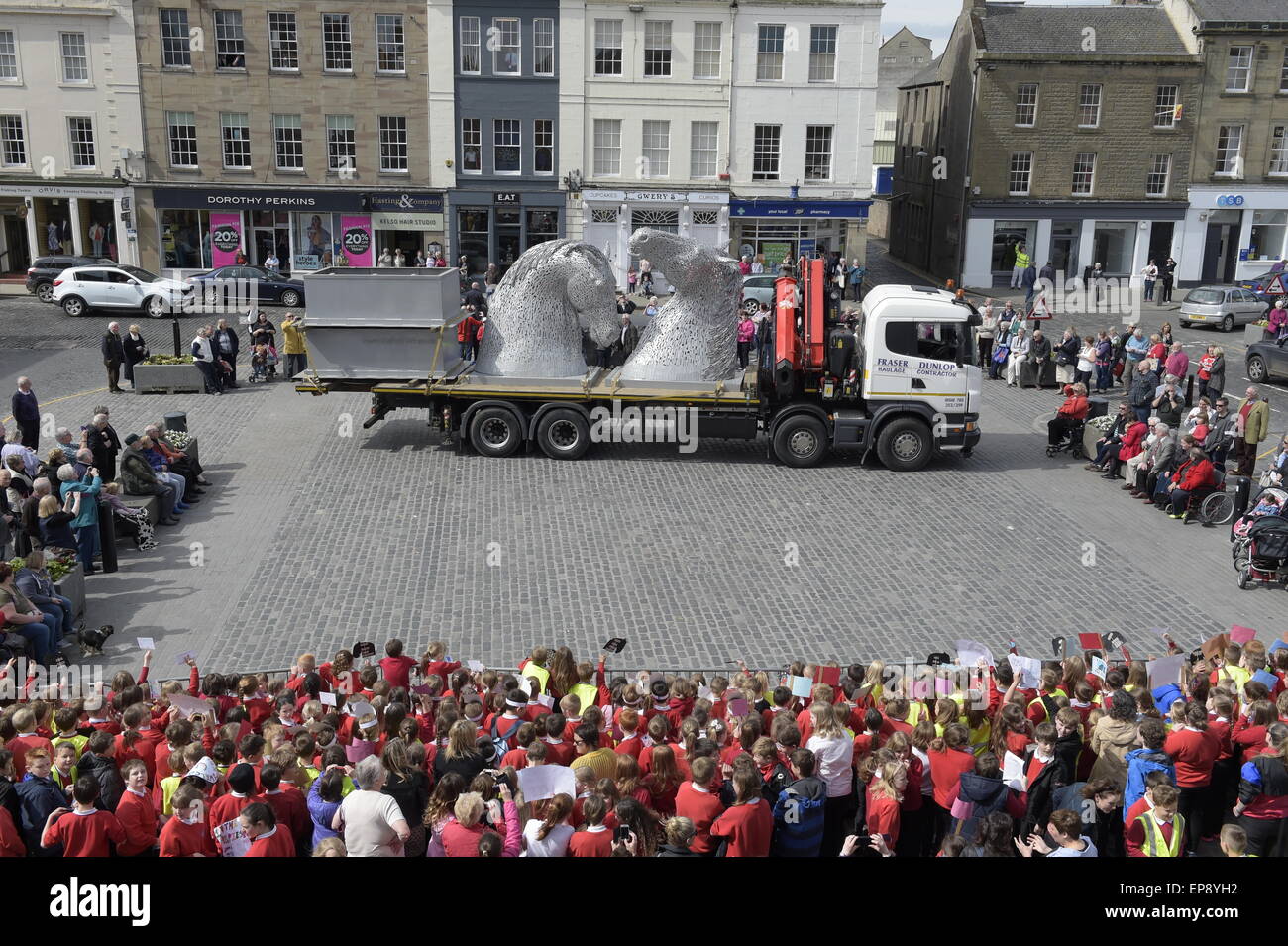 Kelso, Scotland, Regno Unito. Il 15 maggio 2015 tre metri Kelpies elevata per essere stabulati in Kelso quadrato di un decimo di scala touring Kelpies sculture di arrivare in piazza a Kelso venerdì 15 maggio, con studenti locali da Broomlands e Edenside scuole primarie accogliente il loro arrivo. L'iconico sculture rimarrà in posizione al centro della città fino a lunedì 18 maggio. Ciò coincide con un weekend intenso in città e con il castello di pavimenti Horse Trials e la frontiera Vintage associazione agricola annuale del rally a Springwood Park di prendere posto. Credito: Rob grigio/Alamy Live News Foto Stock