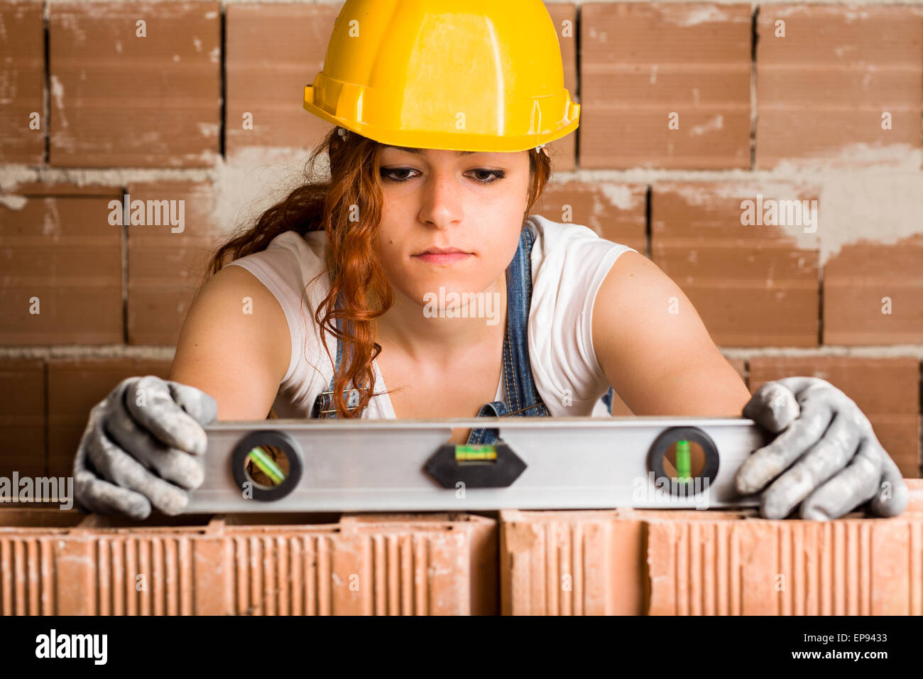 Donna Muratore con casco tenendo un livello di spirito su di un muro di mattoni Foto Stock