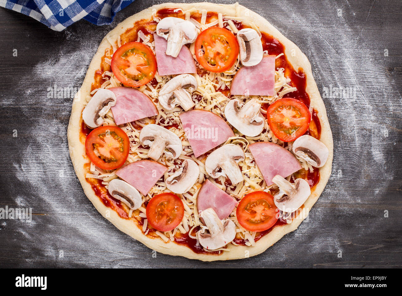 Realizzazione della pizza. Salsa, formaggio, funghi, prosciutto e pomodori in un impasto Foto Stock