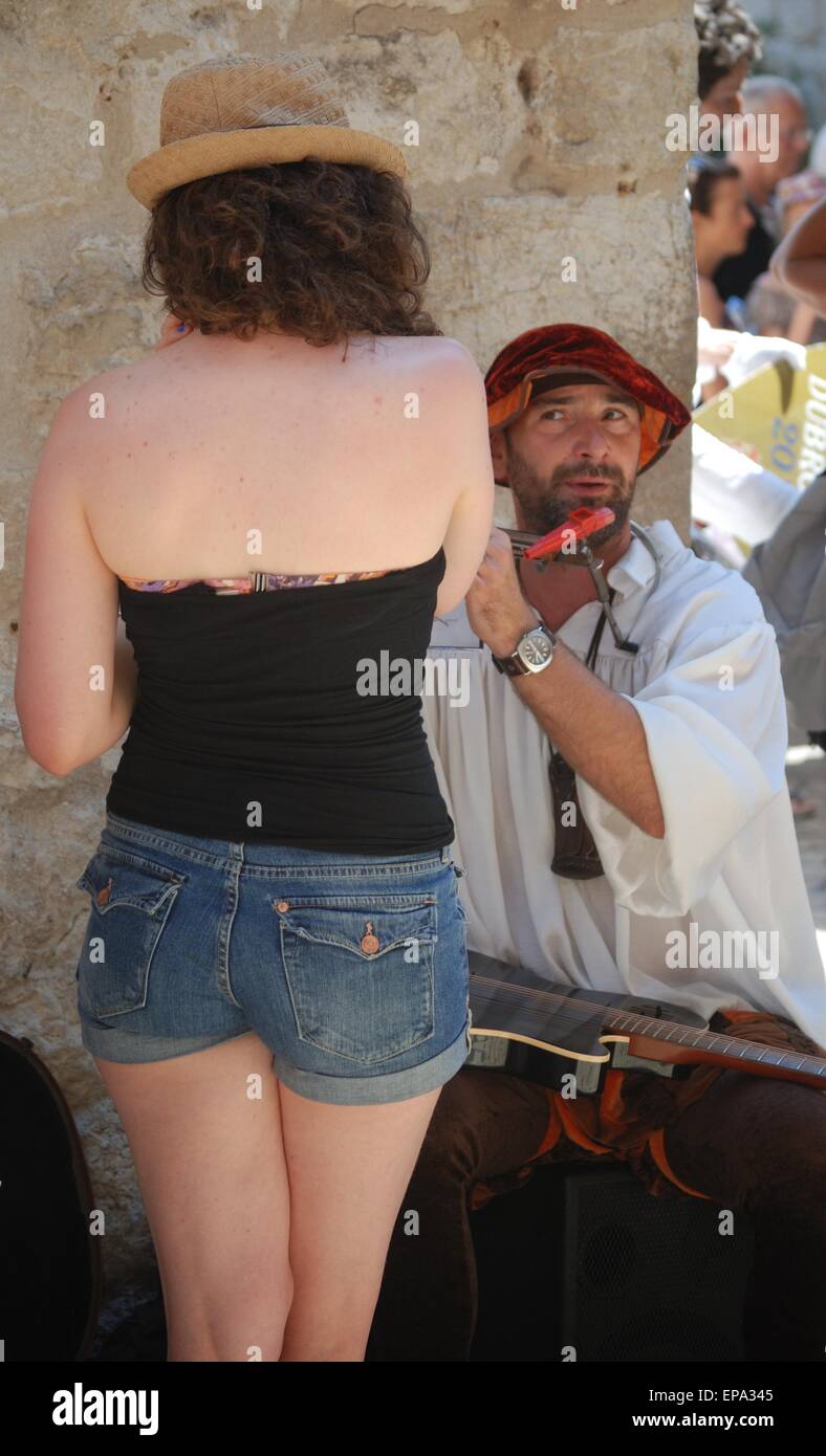 Busker che gioca un flauto nella vecchia strada di Dubrovnik, Croazia. Attraente giovane donna turista che guarda. Foto Stock