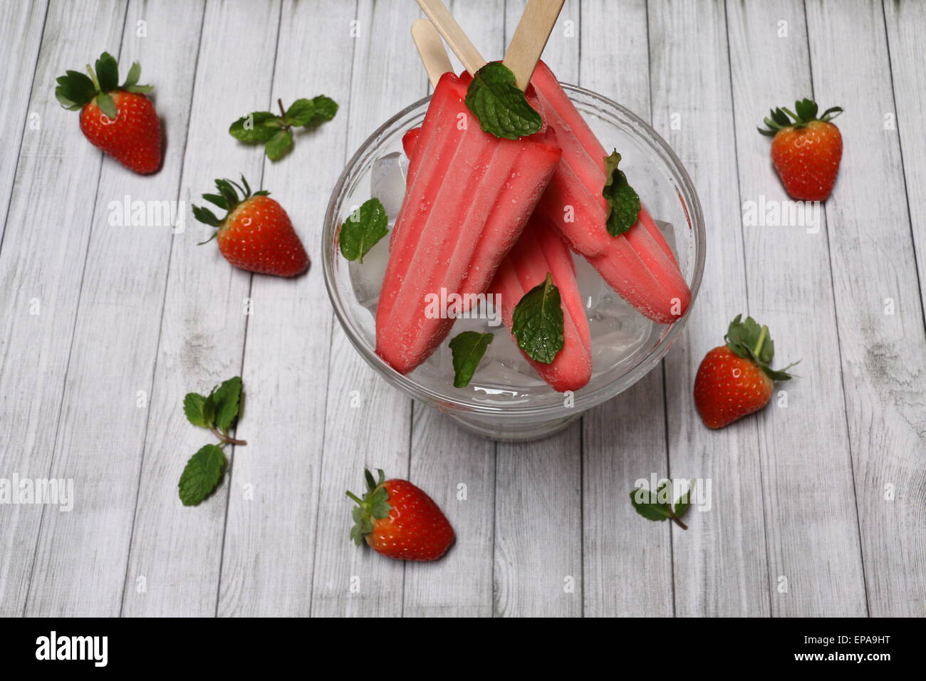 Fragola per lecca-lecca di ghiaccio su letto di cubetti di ghiaccio, guarnito con fragole e foglie di menta su tavola in legno rustico Foto Stock
