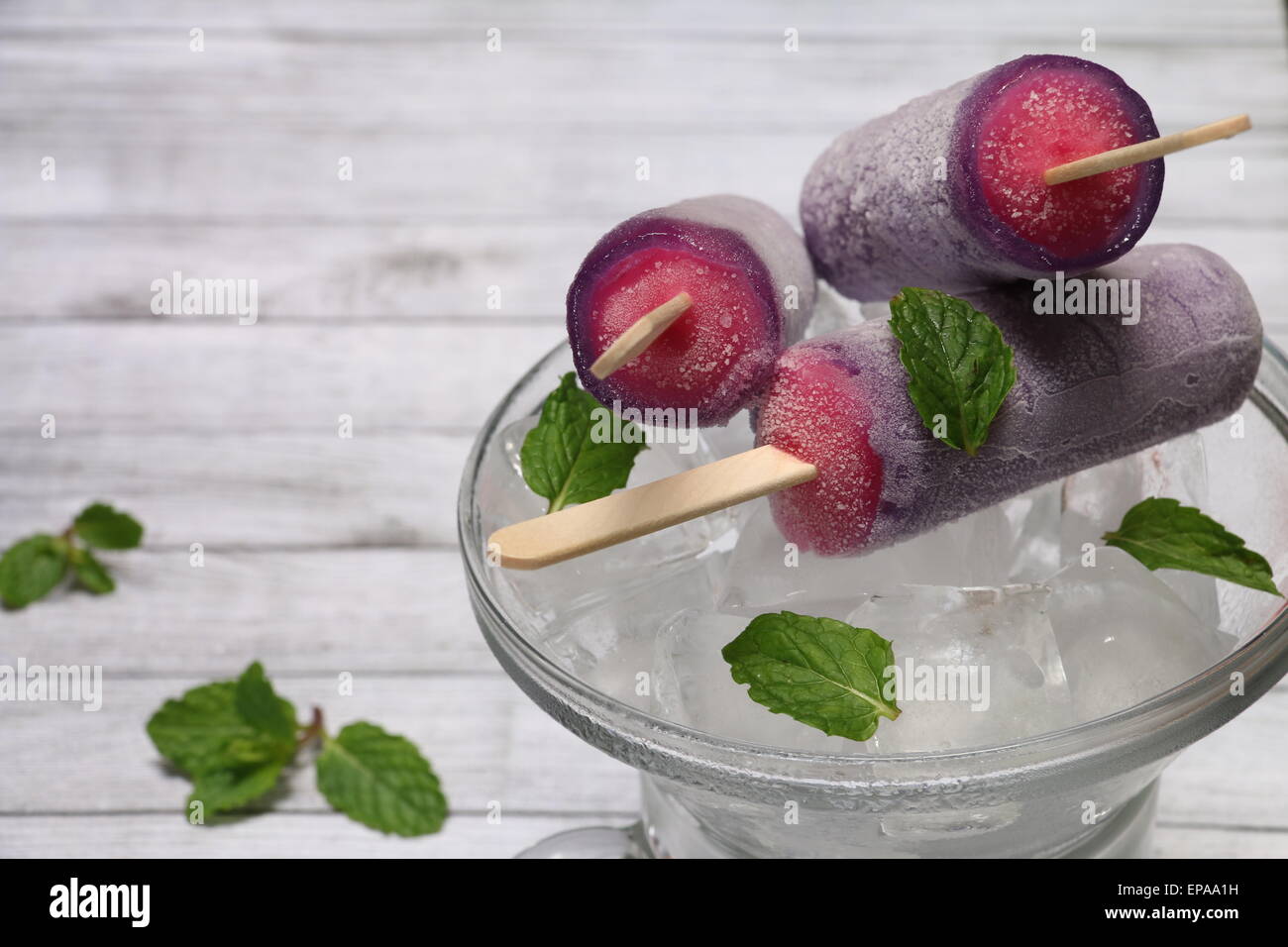 La fragola e uva ghiaccioli su letto di cubetti di ghiaccio, guarnite con foglioline di menta rustico di legno Foto Stock