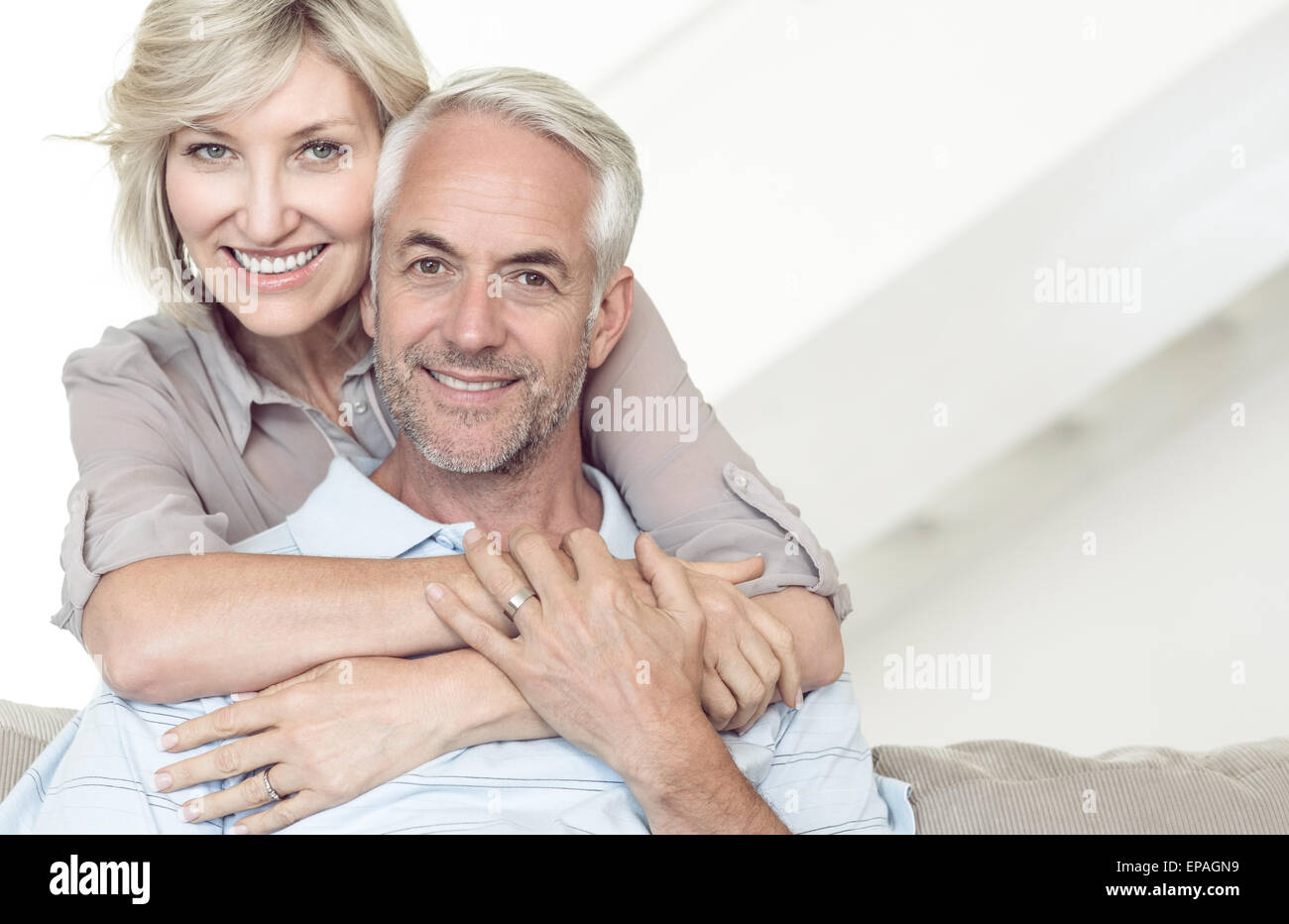 Donna sorridente abbracciando uomo maturo da dietro sul divano Foto Stock