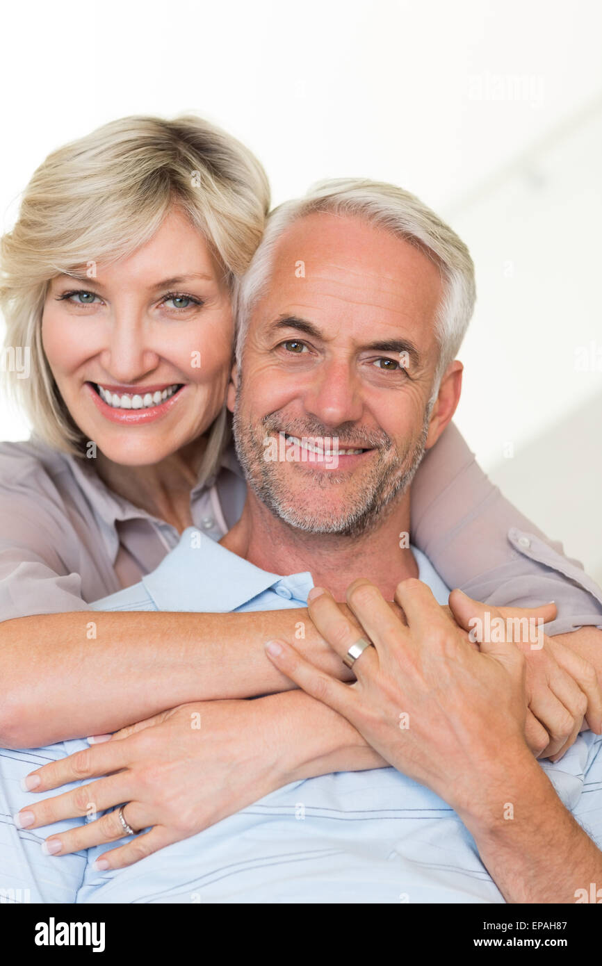 Donna sorridente abbracciando uomo maturo da dietro sul divano Foto Stock