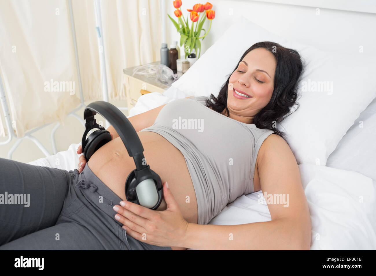 Donne incinte donna mettendo le cuffie sul suo ventre Foto Stock