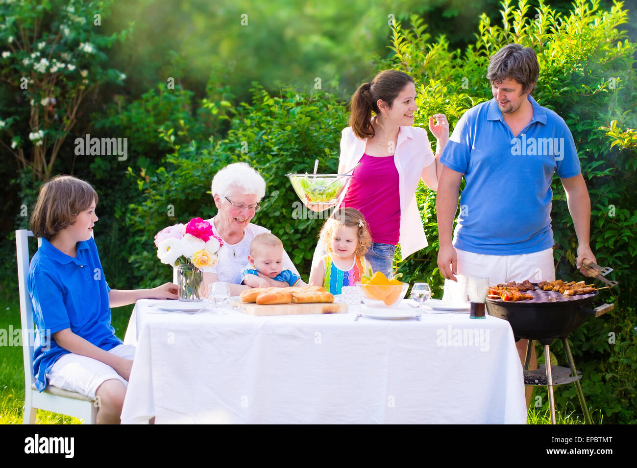 Grill barbecue party nel cortile. Felice famiglia grande godendo di pranzo a barbecue con la nonna di mangiare carne alla griglia nel giardino con insalata Foto Stock
