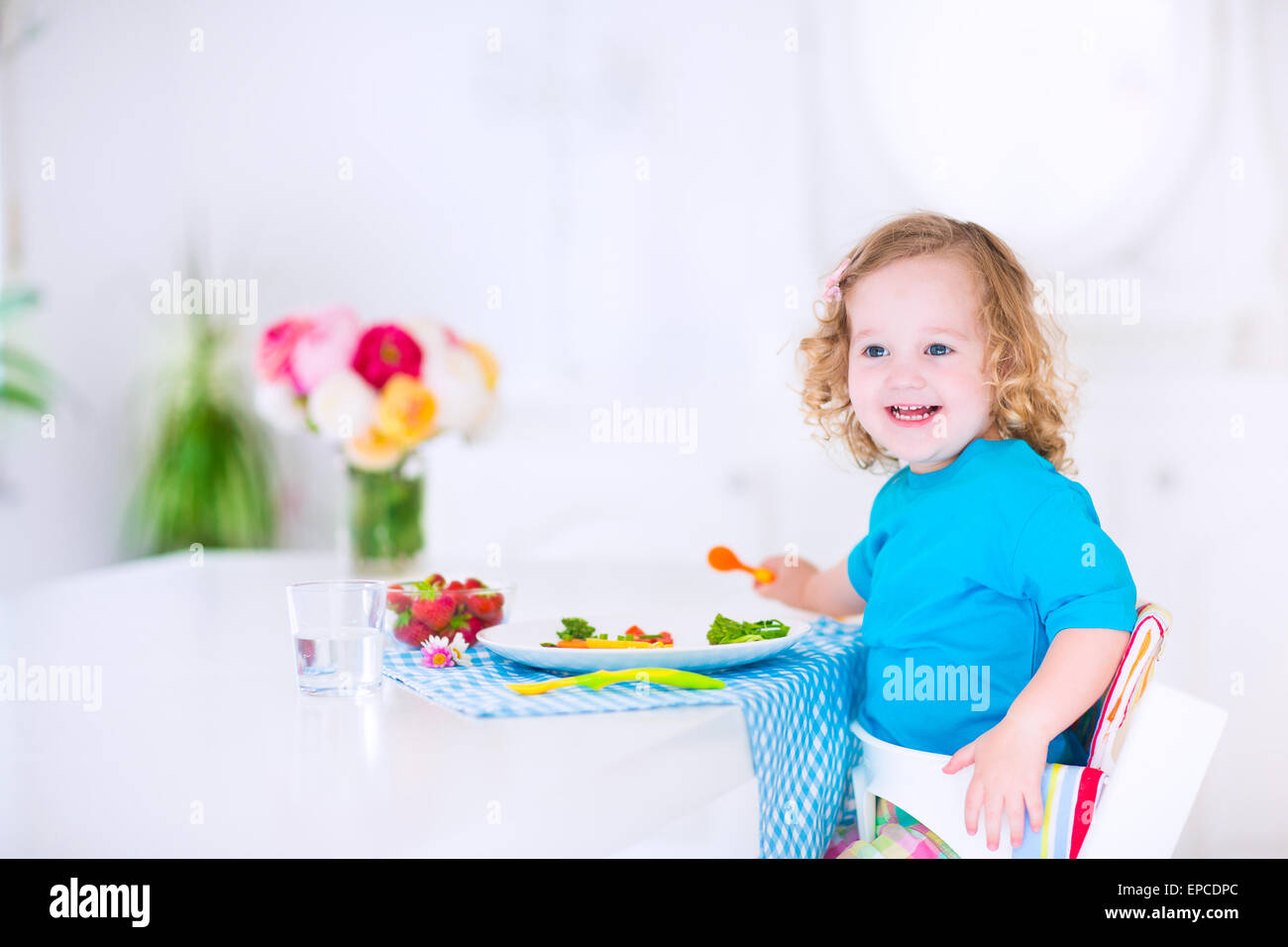 Felice bambina carina toddler ricci, mangiare verdura fresca per il pranzo, insalata di sani snack, mais, broccoli, carote Foto Stock