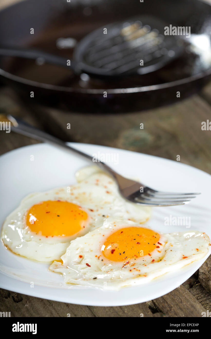 Due uova fritte per una sana prima colazione nella piastra bianca e una padella in background Foto Stock