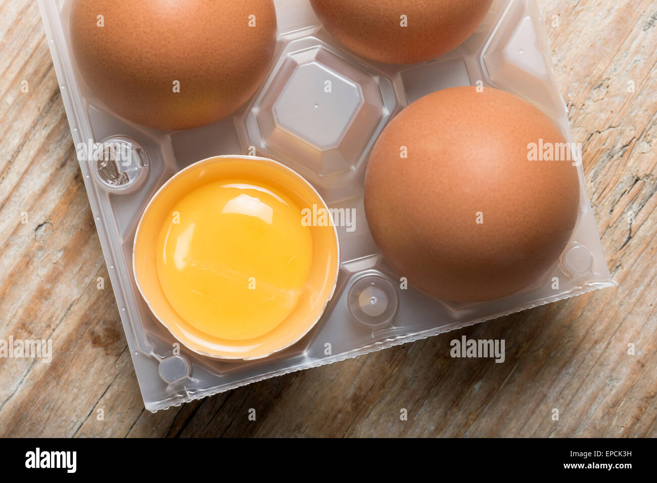 Gruppo di uova con uno aperto con tuorlo d'uovo in cesto in plastica sul tavolo di legno Foto Stock