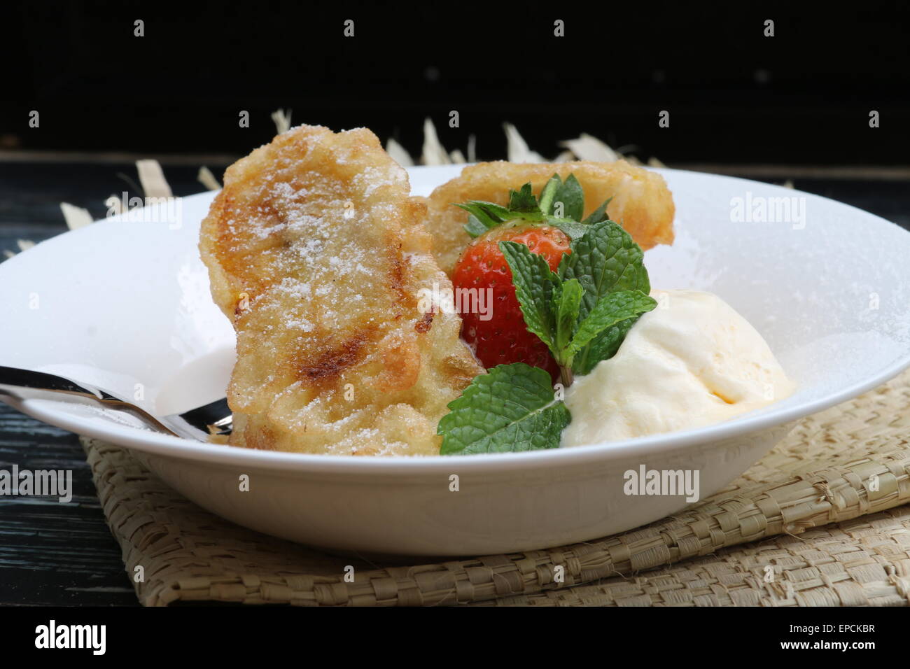 Tre pezzi di impasto-banane fritte con gelato alla vaniglia sulla piastra bianca. Su tavola in legno rustico e stuoia di paglia Foto Stock