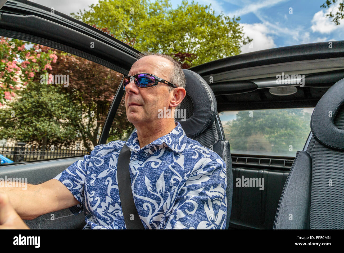 Un uomo di mezza età alla guida di una vettura Cabriolet con il tetto verso il basso in un giorno di estate in Londra England Regno Unito Foto Stock