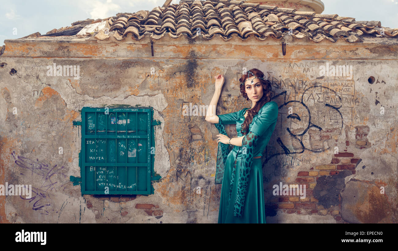 Le belle donne che indossano greca tradizionale di color verde abito in posa mentre appoggiata sulla parete scrawled. Instagram dallo stile del filtro. Foto Stock