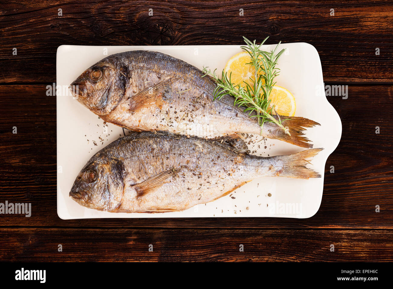 Deliziose grigliate di Orate di mare Pesce sulla scheda cucina con rosmarino, limone e pepe colorato in marrone legno testurizzata Foto Stock