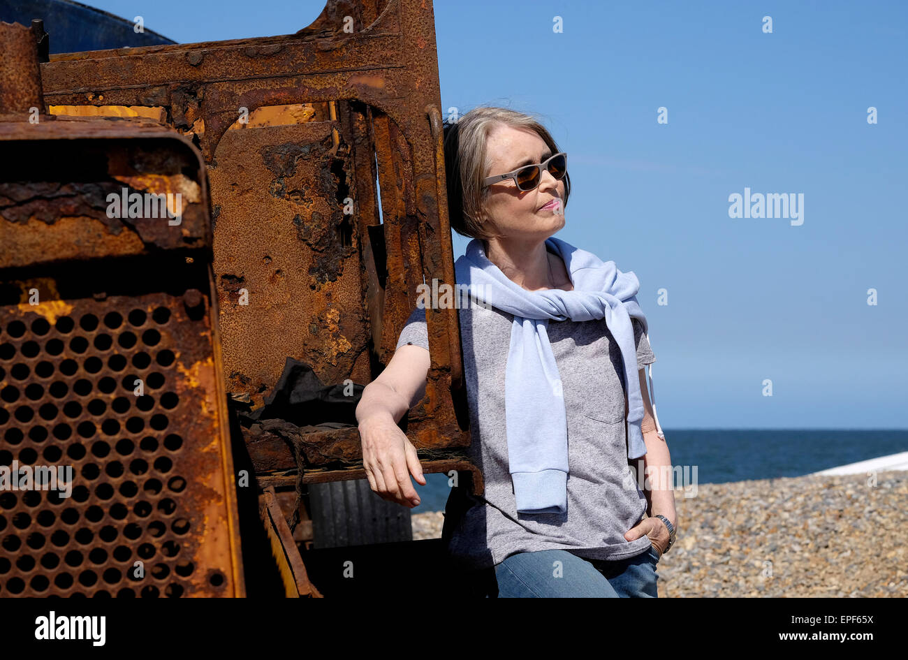 Senior donna appoggiata sul trattore arrugginito sulla spiaggia Foto Stock