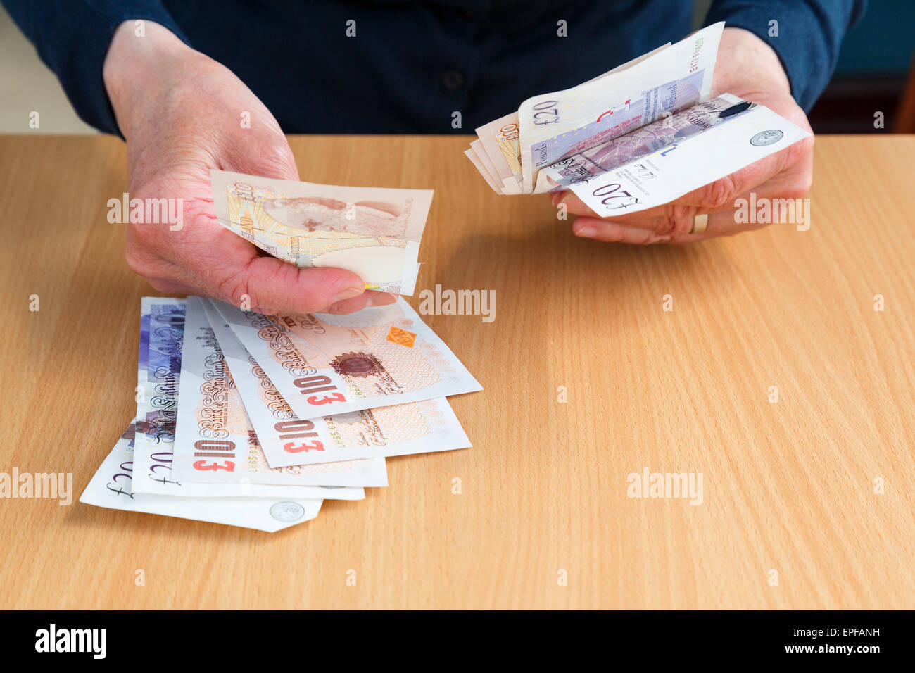 La mano di una persona anziana che tiene i soldi inglesi in sterline dieci e venti sterline banconote GBP per comprare e pagare le libbre contanti sopra un contatore. Inghilterra Regno Unito Foto Stock