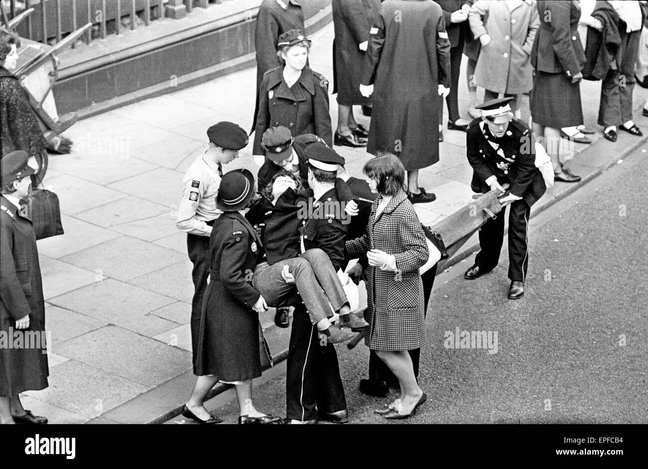 Premier di 'una dura giornata di Notte', la folla si riuniscono per avvistare dei Beatles prima del nord del premier inizia a Liverpool. Una ventola svenuti è trasportato lontano dalla folla per una barella in attesa. Il 10 luglio 1964. Foto Stock