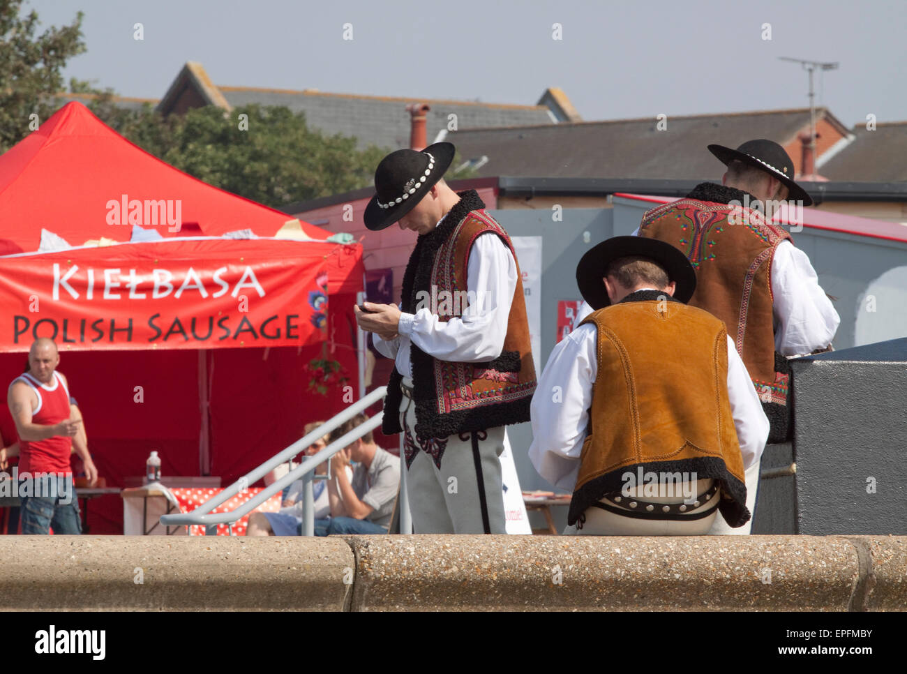 Tre giovani uomini in tradizionale costume polacco controllare i loro telefoni cellulari al 2011 Polacco Arts Festival di Southend Foto Stock