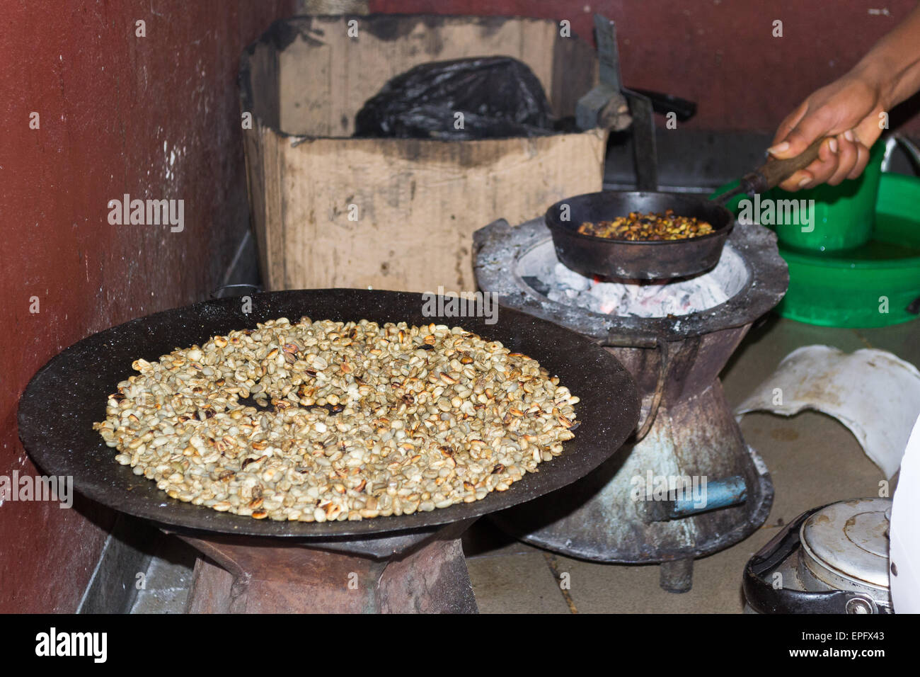 Persona etiope eseguendo una tradizionale cerimonia di caffè, tostatura i chicchi di caffè in una pentola posta su un fuoco di carbone. Indoor. Foto Stock