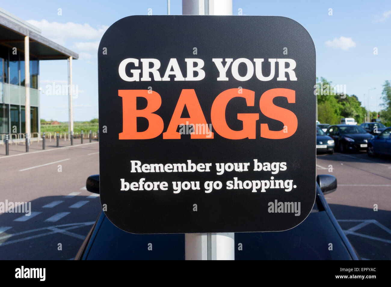 Un segno in un supermercato parcheggio auto per ricordare le persone a prendere le borse della spesa con loro. Foto Stock