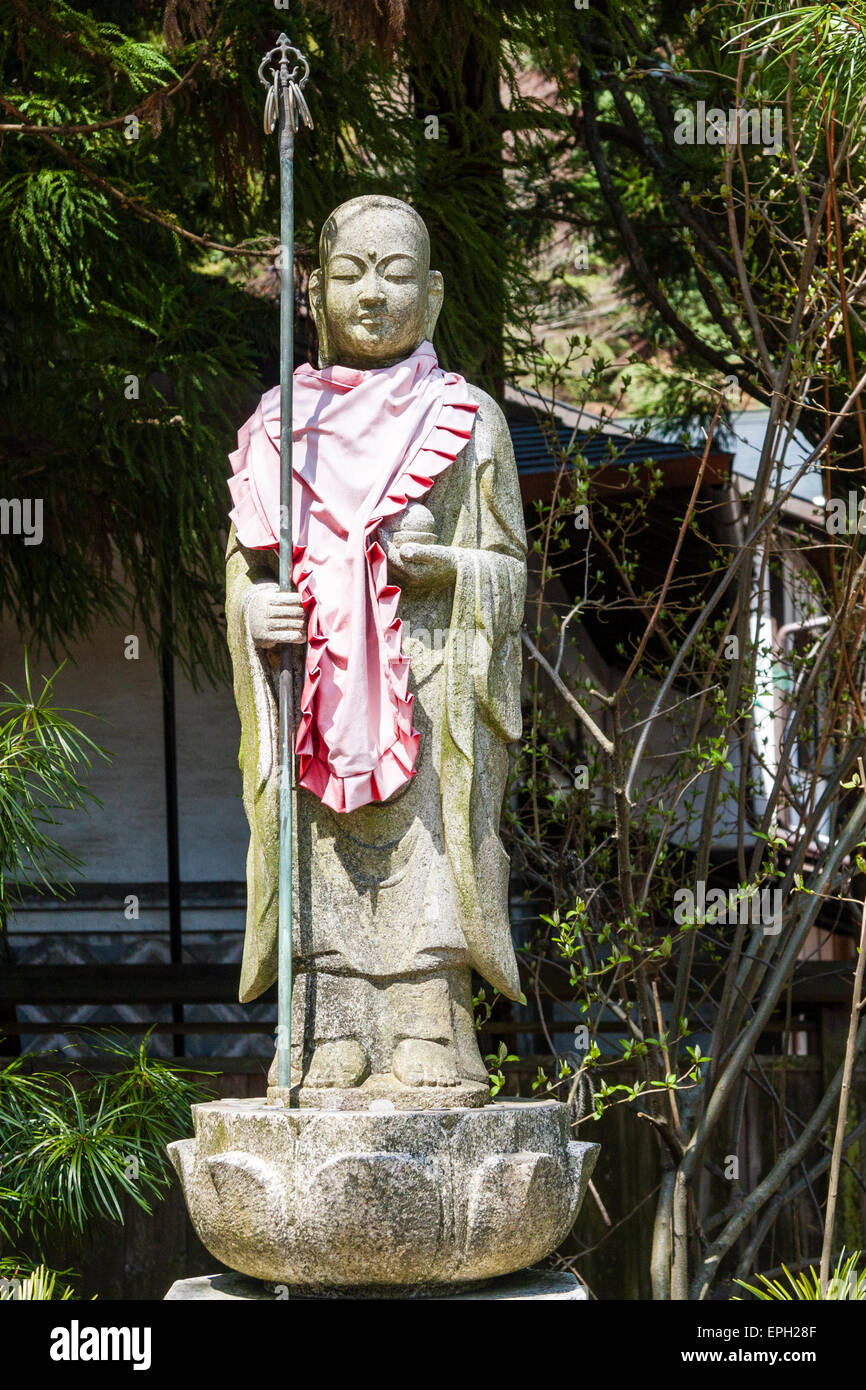 Jizo boddhisatva, bosatsu, statua con orb e staff, shakujo, in piedi su una base di pietra di loto in piena luce del sole in un tempio, Koyasan, Giappone Foto Stock