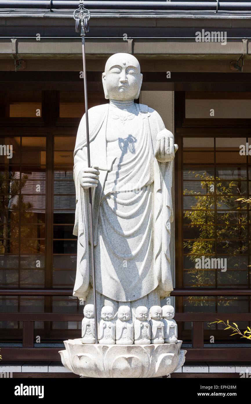 Jizo boddhisatva, bosatsu, statua con orb e staff, shakujo, in piedi sulla base di piccole statue jizo in piena luce del sole in un tempio a Koyasan, Giappone. Foto Stock