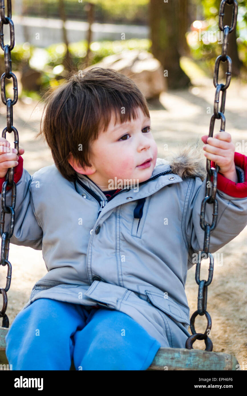 Bambino angelico, ragazzo di 3-4 anni, che gioca su un'altalena in un  parco. Indossa un cappotto invernale e ha guance rosse a causa del freddo  Foto stock - Alamy