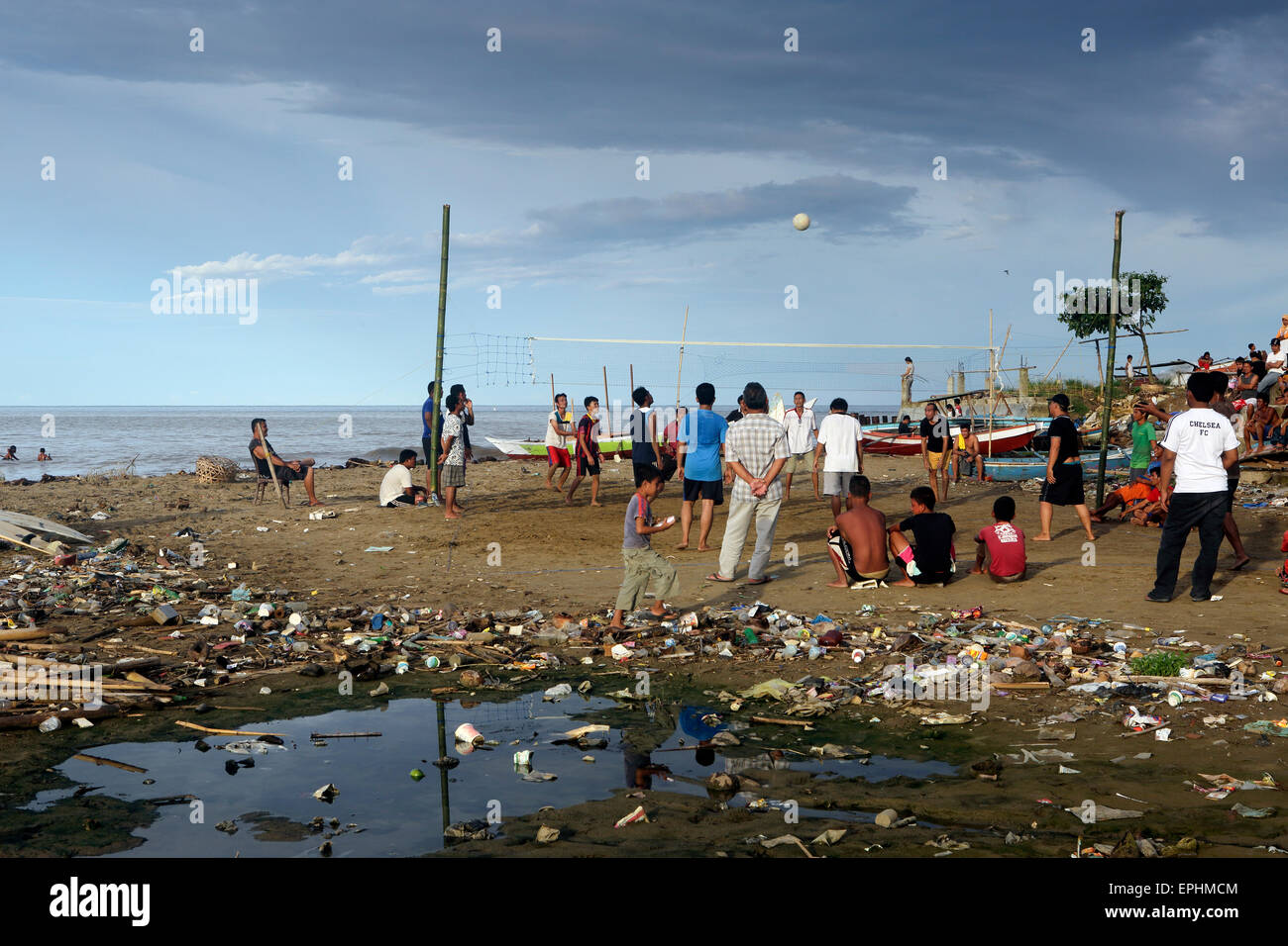 Gli uomini che giocano una partita di pallavolo sulla spiaggia coperta di immondizia di plastica e di altri rifiuti di Sumatra, Indonesia Foto Stock