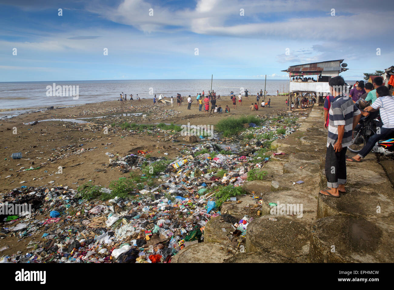 Gli uomini che giocano una partita di pallavolo sulla spiaggia coperta di immondizia di plastica e di altri rifiuti di Sumatra, Indonesia Foto Stock