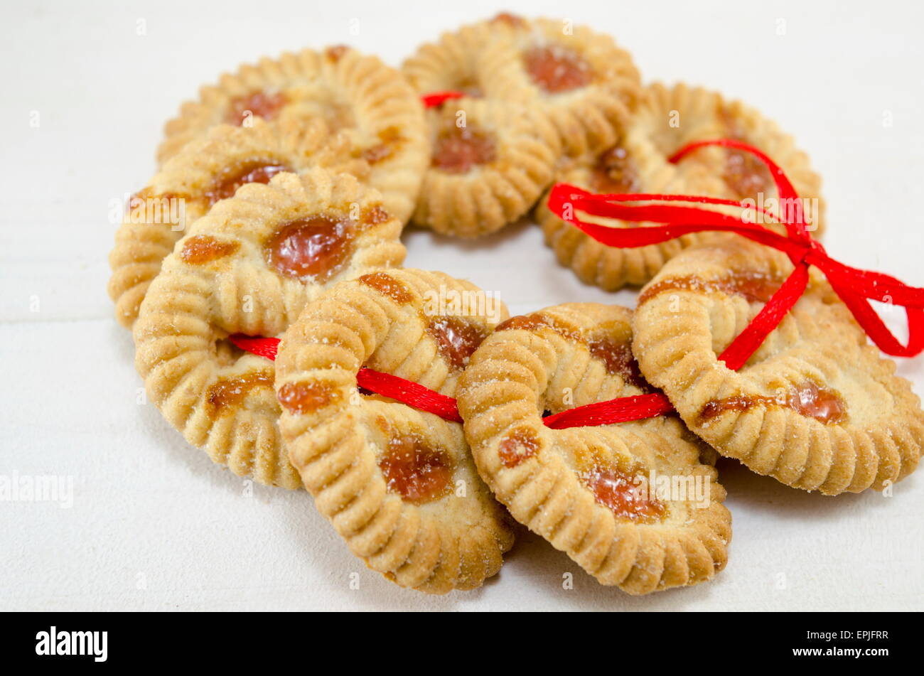 Biscotti da tè riempita con marmellata di albicocche su bianco collegato con un nastro rosso Foto Stock