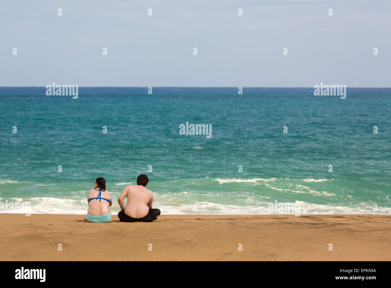 Il sovrappeso caucasian giovane seduto sulla spiaggia Foto Stock