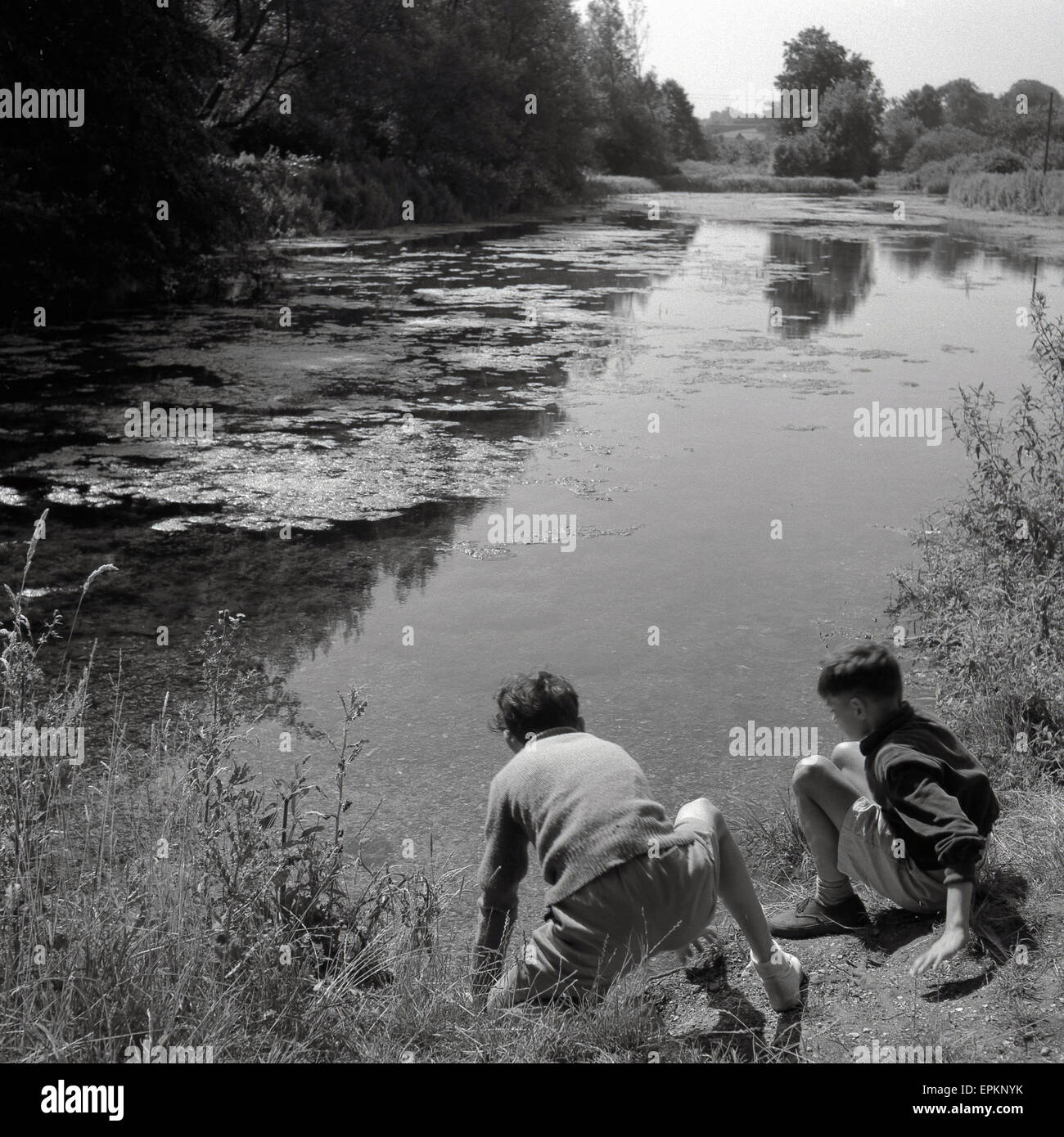 Anni '50, storico, estivo e due ragazzi al di fuori del paese giocano accanto a un fiume poco profondo, Inghilterra, Regno Unito. Foto Stock