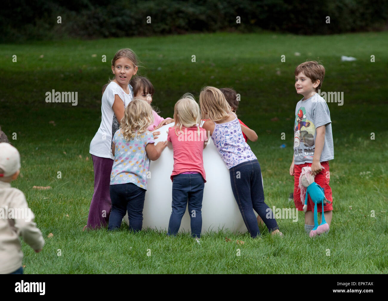 Bambini clustered round una gigantesca sfera bianca in un parco Foto Stock