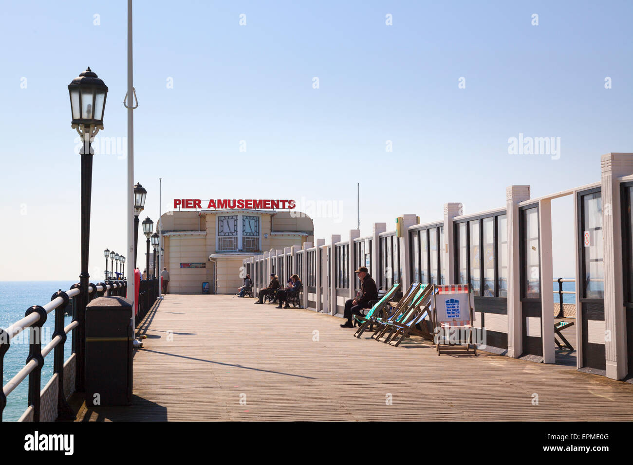 Le persone sedute a Worthing Pier dietro il vetro frangiventi e Pier Amusements segno Foto Stock