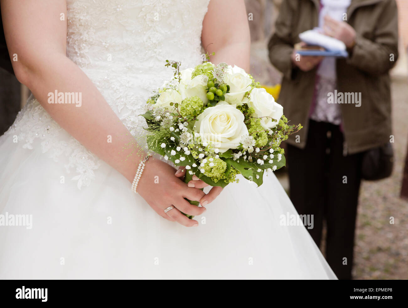 Una sposa in bianco di un abito da sposa tenendo un bouquet nuziale con Rose in mano Foto Stock