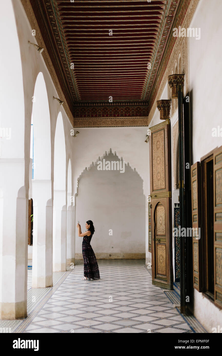Una donna in un nero abito fluente richiede un iphone Immagine nel cortile di Palazzo Bahia, Marrakech Foto Stock