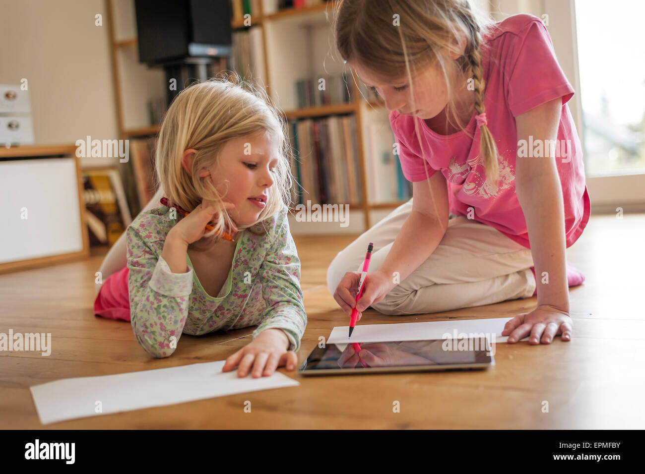 Due sorelle con tavoletta digitale e dei fogli di carta sul pavimento Foto Stock