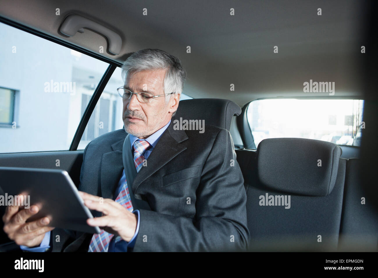 Imprenditore seduto in un auto con tavoletta digitale Foto Stock