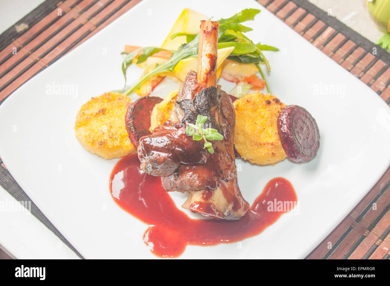 Una piastra piena di gambo di agnello, salsa al vino rosso, polenta, la barbabietola e insalata mista Foto Stock