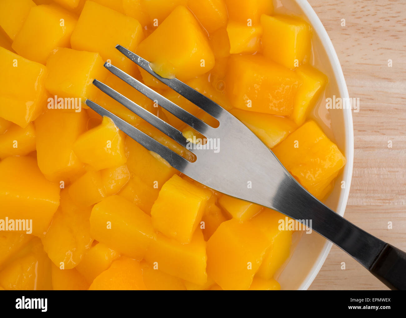 Top vista ravvicinata di un serving di conserve di dadini di mango in un piccolo piatto con una forcella su una tavola di legno alto. Foto Stock