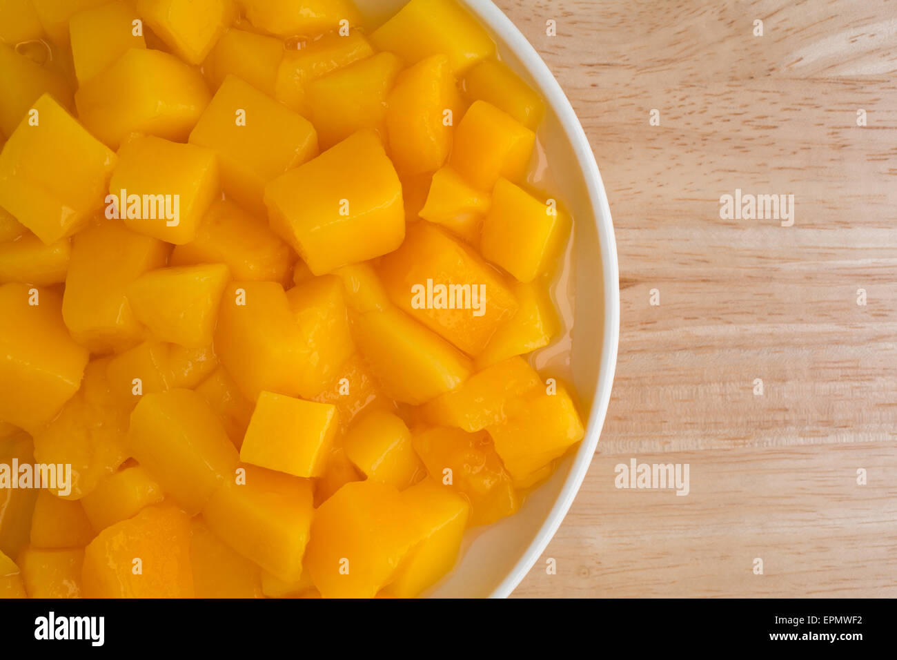 Top vista ravvicinata di un serving di conserve di dadini di mango in un piccolo piatto in cima a una tavola di legno alto. Foto Stock