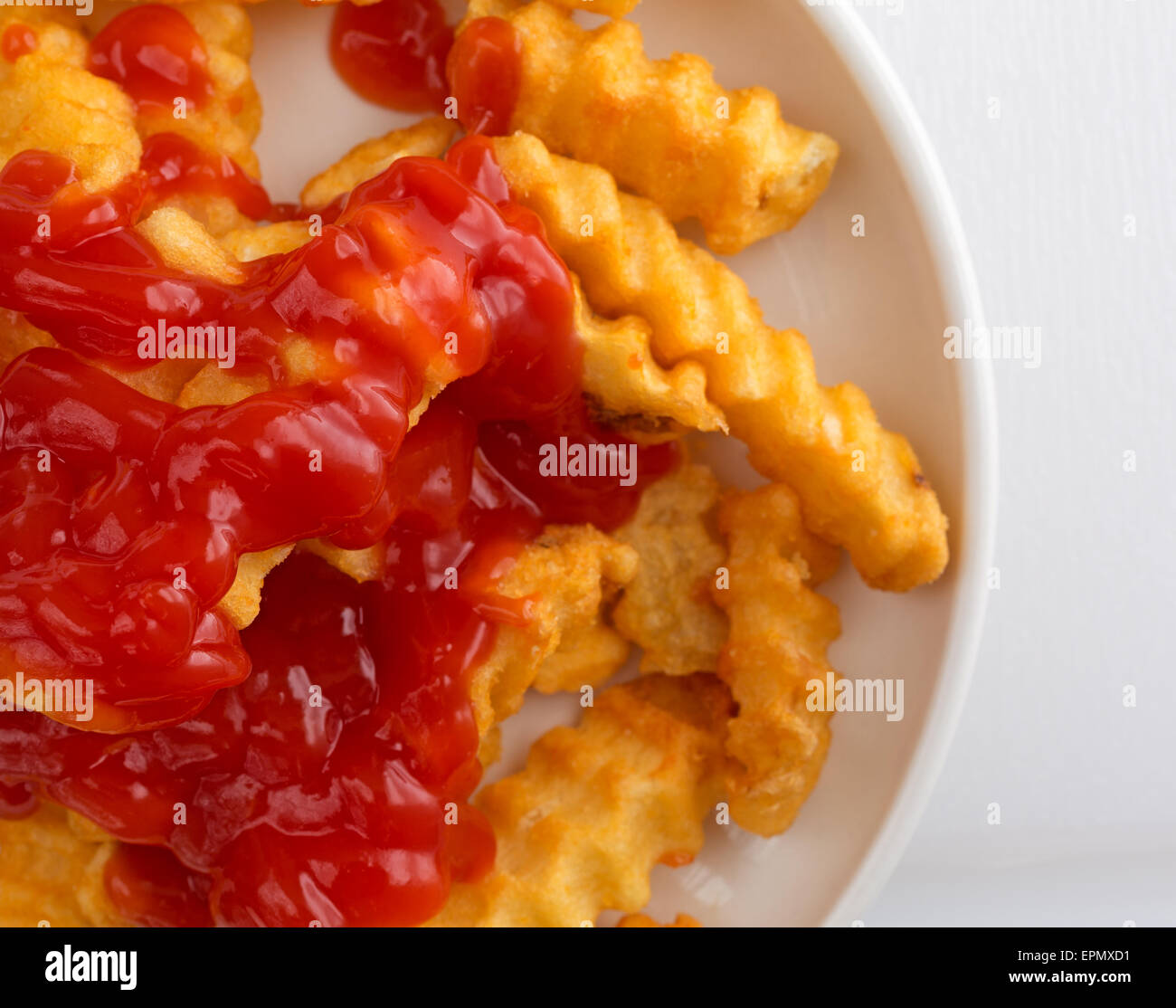 Vista ravvicinata di Croccanti patatine fritte coperto con ketchup in un piccolo piatto su un tavolo bianco alto. Foto Stock