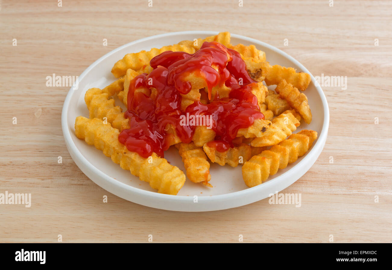 Croccanti patatine fritte coperto con ketchup in una piccola piastra su una tavola di legno alto. Foto Stock